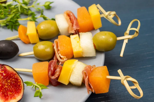 Peynirli şişler, zeytinler ve gri tabakta jamon. Kapatın. Mavi arkaplan.