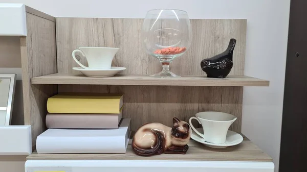 Kitaplarla dolu bir raf, bir bardak ve bir heykel..