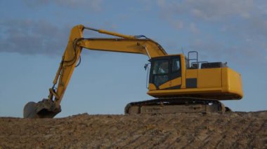 İnşaat alanı kazıcısı ağır kürek sarı hidrolik ekipman toprak kazıcı zaman kaybı mavi gökyüzü ve bulutlar