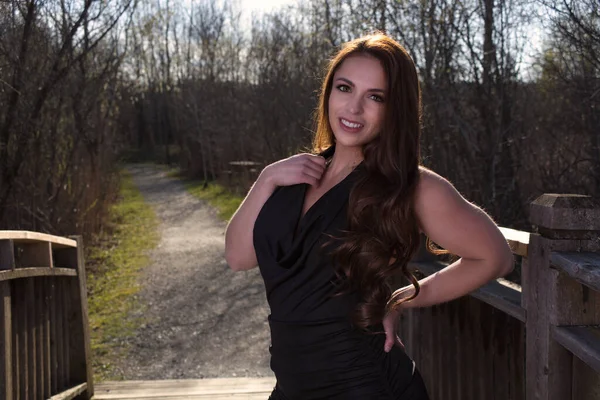 Gülümseyen genç bir kadın, bahar parkında poz veriyor. Siyah bir elbise giyiyor.