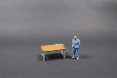 Gri arka planda masası olan küçük iş adamı figürü 