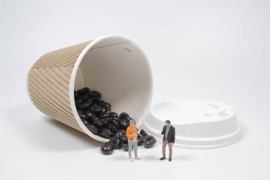 Kahve çekirdekleri dökülmüş fincanla insanların mini figürleri.