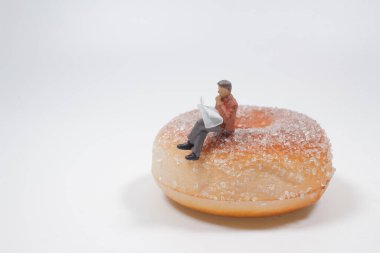 Şekil adamı büyük bir çöreğin üzerine oturur gazete okur.