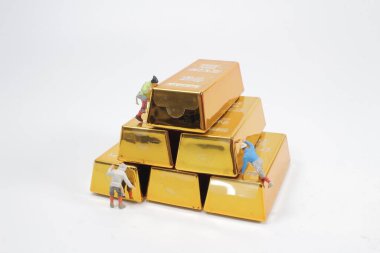 Altın külçesine tırmanan mini figür.