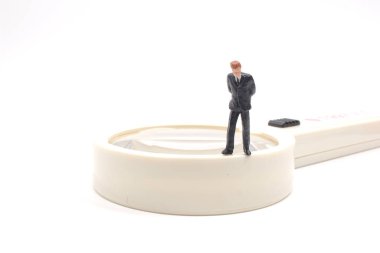 Beyaz panoda büyüteç ve minyatür insanlar var.