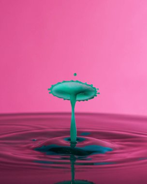 Pembe arka planda yeşil su damlaları çarpışması. Yüzeyde bir su damlası..