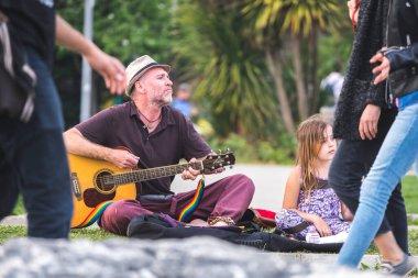 Olgun adam gitar çalıyor ve küçük kız da onu parkta çimlerin üzerinde dinliyor..