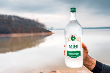 İki litre Yunan anasonlu alkollü içecek taşıyan bir erkeğin eli gölün arka planında bulanıklaştı..