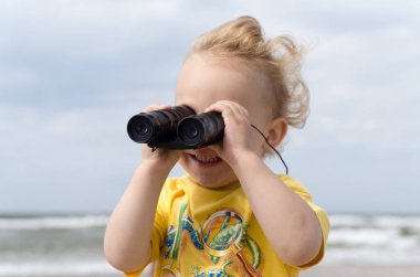 Çocuk sahilde dürbünle bakıyor.