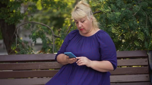 뚱뚱 한 여자는 벤치에 앉아 스마트폰을 사용 한다 — 비디오