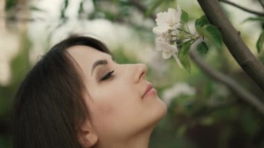 Genç bir kadın ağaçta çiçek kokluyor.