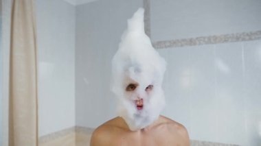 Sabunlu köpüklü bir adam banyoda dans ediyor.