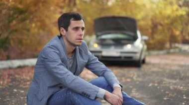 Bozuk bir arabanın önündeki adam.