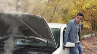 Bozuk arabanın yanında üzgün bir adam var.