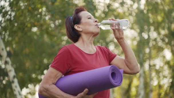 Femme âgée avec tapis de yoga boissons eau — Video