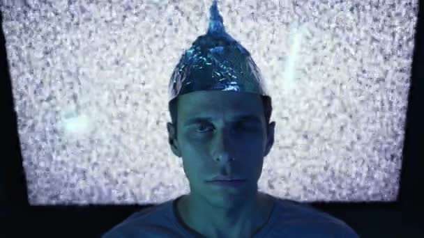 Man met een hoed van aluminiumfolie in de voorkant van de tv. — Stockvideo