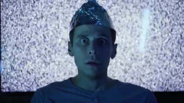 Scared man wearing tin foil hat in a front of TV screen — Stock Video