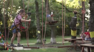 Çocuk parkta ip köprüde yürüyor.