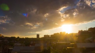 Şehir manzarasında dramatik bir gün batımı zamanı kabarık bulutlar, yağmur ve mavi gökyüzünde altın güneş.