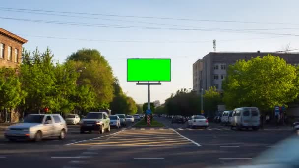 도시의 교통, 걷는 사람, 나무, 건물, 푸른 하늘을 배경으로 녹색 화면 이 있는 광고판입니다. 아르메니아의 도시 예레반에서. 다가오는 카메라 — 비디오