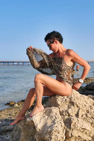 Женжина в купальнику на березі моря, сидячи на каміннях, виражає почуття задоволення.. — стокове фото