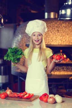 Ellerinde sebzelerle aşçı gibi giyinmiş küçük kız..