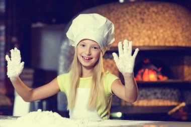 Fırıncı kıyafetli, güzel bir gülümsemesi olan, unla çalışan, küçük neşeli kız, elini un içinde gösteriyor.