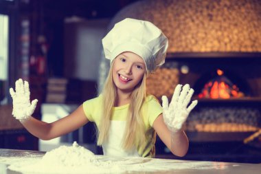 Fırıncı kıyafetli, güzel bir gülümsemesi olan, unla çalışan, küçük neşeli kız, elini un içinde gösteriyor.