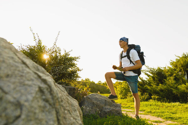 Путешественник средних лет с большим рюкзаком на плечах, который находится в парке, внимательно смотрит на карту.