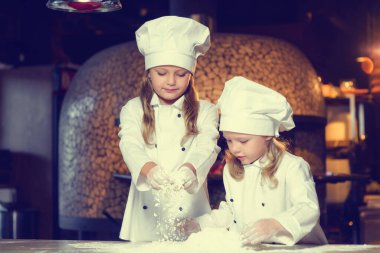 Beyaz aşçı üniformalı iki kız mutfakta unla oynuyorlar..
