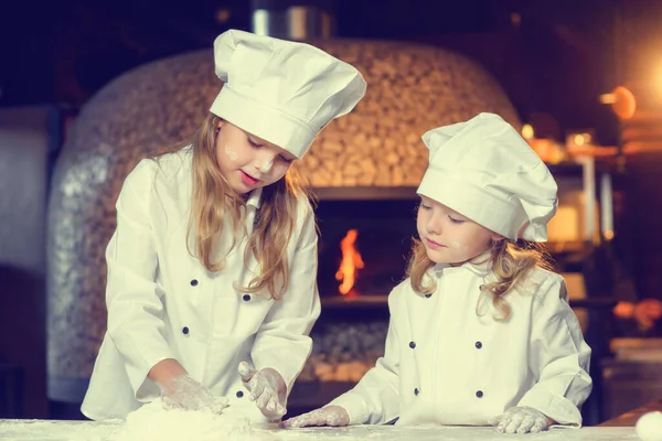 Deux petites filles gaies, souillées dans la farine, vêtues d'un uniforme de chefs, préparent un produit à base de farine. — Photo