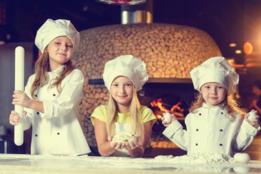Fırının yanında, un içinde ve şef üniforması giymiş üç neşeli küçük kız bir un ürünü hazırlıyorlar..