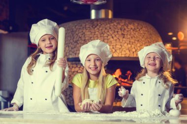 Fırının yanında, un içinde ve şef üniforması giymiş üç neşeli küçük kız bir un ürünü hazırlıyorlar..