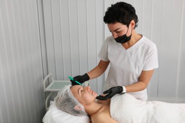 The beautician marks the site of the procedure on the face with a green marker.
