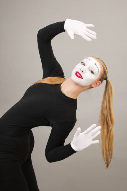 Beautiful girl artist in the role of pantomime gesticulates. Close-up on a gray background.