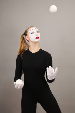 Pandomim sanatçısı toplarla hokkabazlık yapıyor. Sirk palyaçosu kadın. Gri bir arkaplanda.