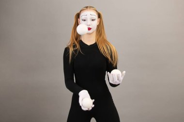 Pandomim sanatçısı toplarla hokkabazlık yapıyor. Sirk palyaçosu kadın. Gri bir arkaplanda.