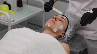 Yetişkin bir kadının yüzüne, güzellik salonundaki cilt yenileme işlemleri için antiseptik krem sürdüm. Yakın plan..