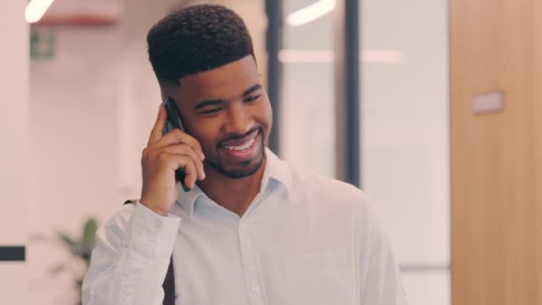 若いビジネスマンがオフィスにいながら携帯電話で話をしていて — ストック動画