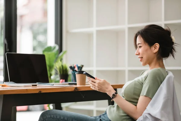 Glad asiatisk kvinna som använder mobiltelefon på modernt kontor — Stockfoto