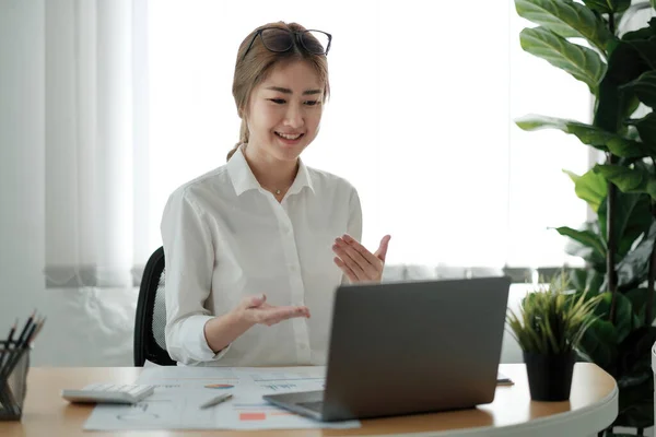 Sonriente joven empleada en casa hablar hablar en videollamada en el ordenador portátil con diversos colegas. Asiática mujer trabajador tener webcam conferencia o digital web team meeting o briefing con compañeros de trabajo — Foto de Stock