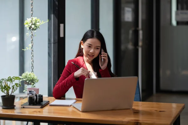 Lächelnde Geschäftsfrau bei der Arbeit telefoniert, Asiatin sitzt und arbeitet mit Laptop — Stockfoto