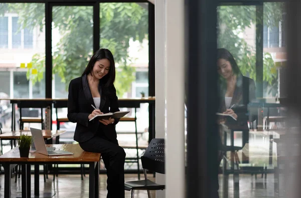 Retrato de bela sorridente jovem empresária que trabalha com computador portátil durante a tomada de nota no bloco de notas — Fotografia de Stock