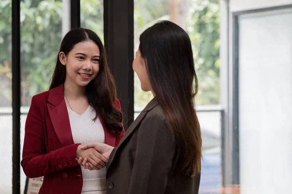 Usmívající se mladá podnikatelka potřásající si rukou se spolupracovnicí během setkání s kolegy u stolu v kanceláři. — Stock fotografie