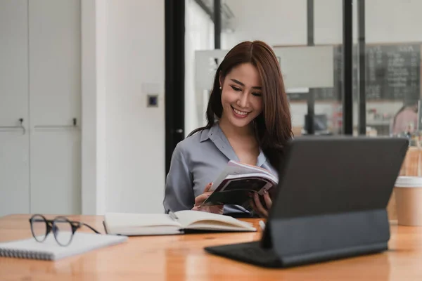 Sorrindo mulher asiática lendo um livro enquanto estudava ou webinar on-line via tablet, conceito de videoconferência — Fotografia de Stock