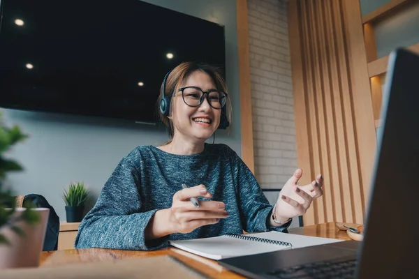 아시아 여성들은 헤드폰을 끼고 노트북 컴퓨터를 보면서 개인 교사와 함께 온라인으로 공부를 즐기고, 음성 강의를 듣고, 시험 준비, 전자 학습, 자아 교육 개념에 대한 음성 강의를 듣는다. — 스톡 사진