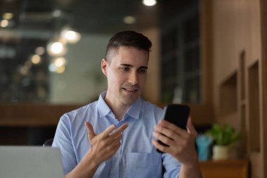 Neşeli mutlu iş adamı sanal iletişim için akıllı telefon uygulaması kullanıyor, telefonu elinde tutuyor ve webcam 'e el sallıyor, masada oturmuş video görüşmesi yapıyor..
