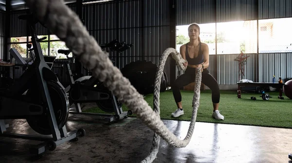 Atractivo fuerte asiática fitness mujer haciendo batalla cuerdas ejercicio en el gimnasio. entrenamiento con pesas sesión de ejercicio — Foto de Stock