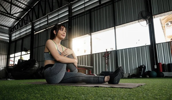 Νεαρή Ασιάτισσα με στυλάτο και άνετο αθλητικό ένδυμα που τεντώνει τα πόδια της στο πάτωμα γυμναστικής. άσκηση και την έννοια του αθλητισμού. Fit γυναίκα κάνει διατάσεις προπόνηση στο γυμναστήριο — Φωτογραφία Αρχείου