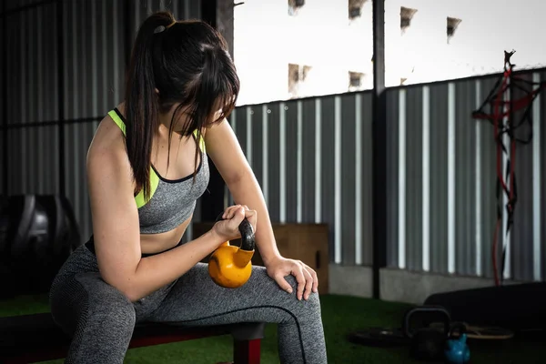 Νεαρή Ασιάτισσα απολαμβάνει την άσκηση με την ανύψωση καμπάνα βραστήρα με το ένα χέρι στο γυμναστήριο. έννοια bodybuilding αθλητισμού. — Φωτογραφία Αρχείου